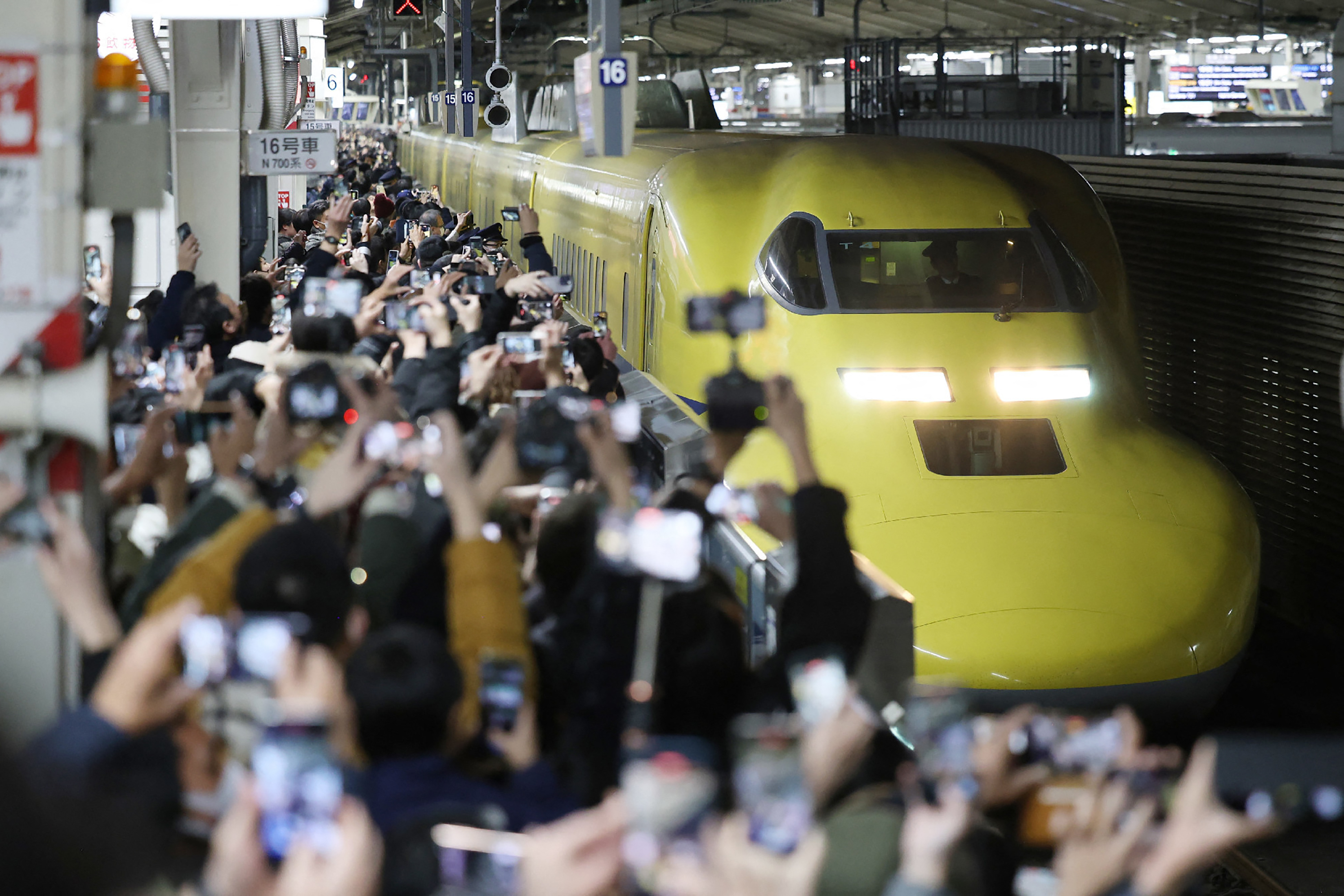 Crowds of people taking pictures of the "Doctor Yellow" shinkansen train arriving at Tokyo Station.