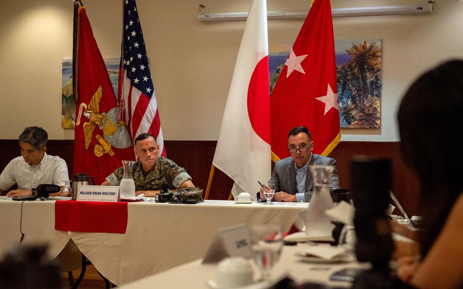 A major general speaks to reporters from a table with American and Japanese flags in the background.
