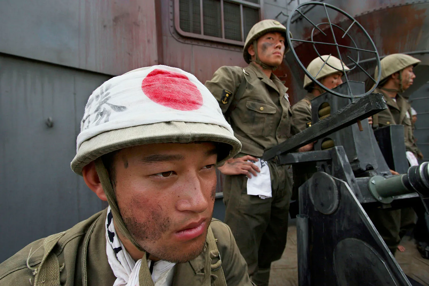 An actor in a uniform with helmet and red circle on it stands next to other actors in military uniforms.