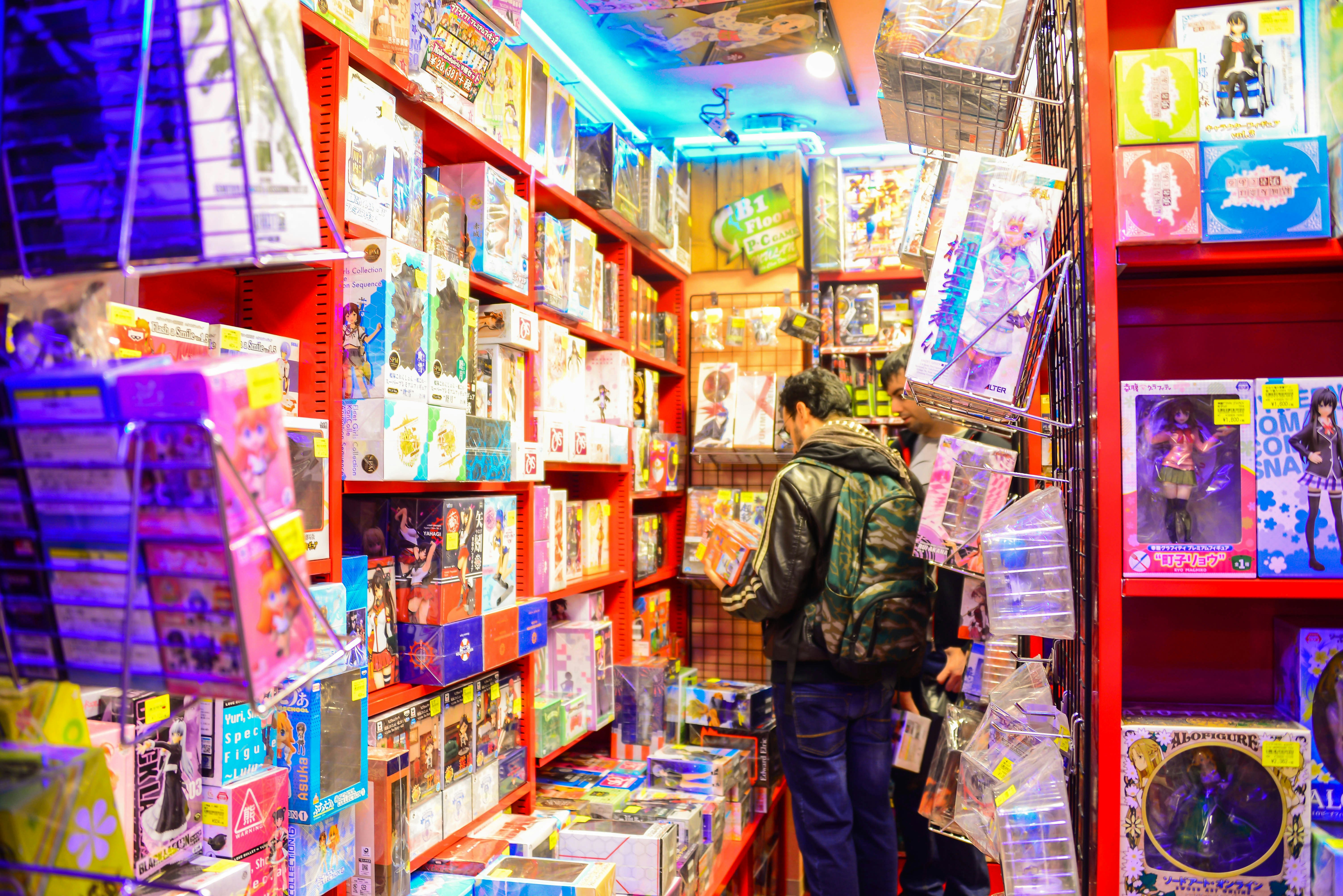 A man browsing in a manga store in Tokyo; the shelves around the shopper are filled with anime-style comics, toys and games.