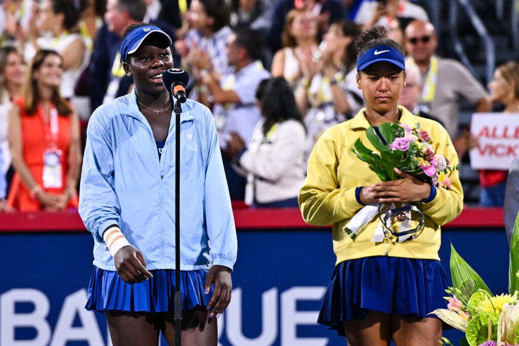 Victoria Mboko speaks into a microphone whilst Naomi Osaka looks downbeat in the background