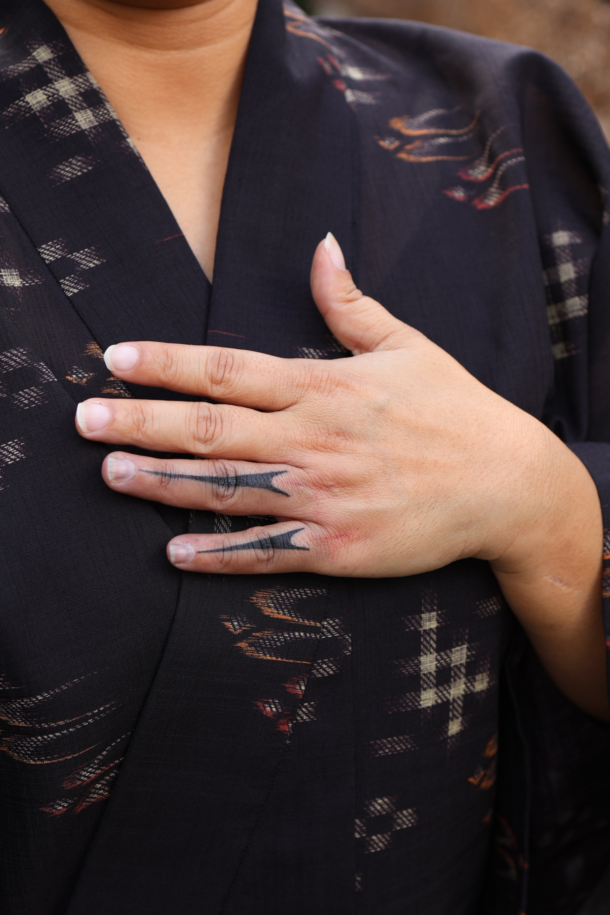 A woman's left hand with triangular spears tattooed across the back of her pinky and ring fingers.