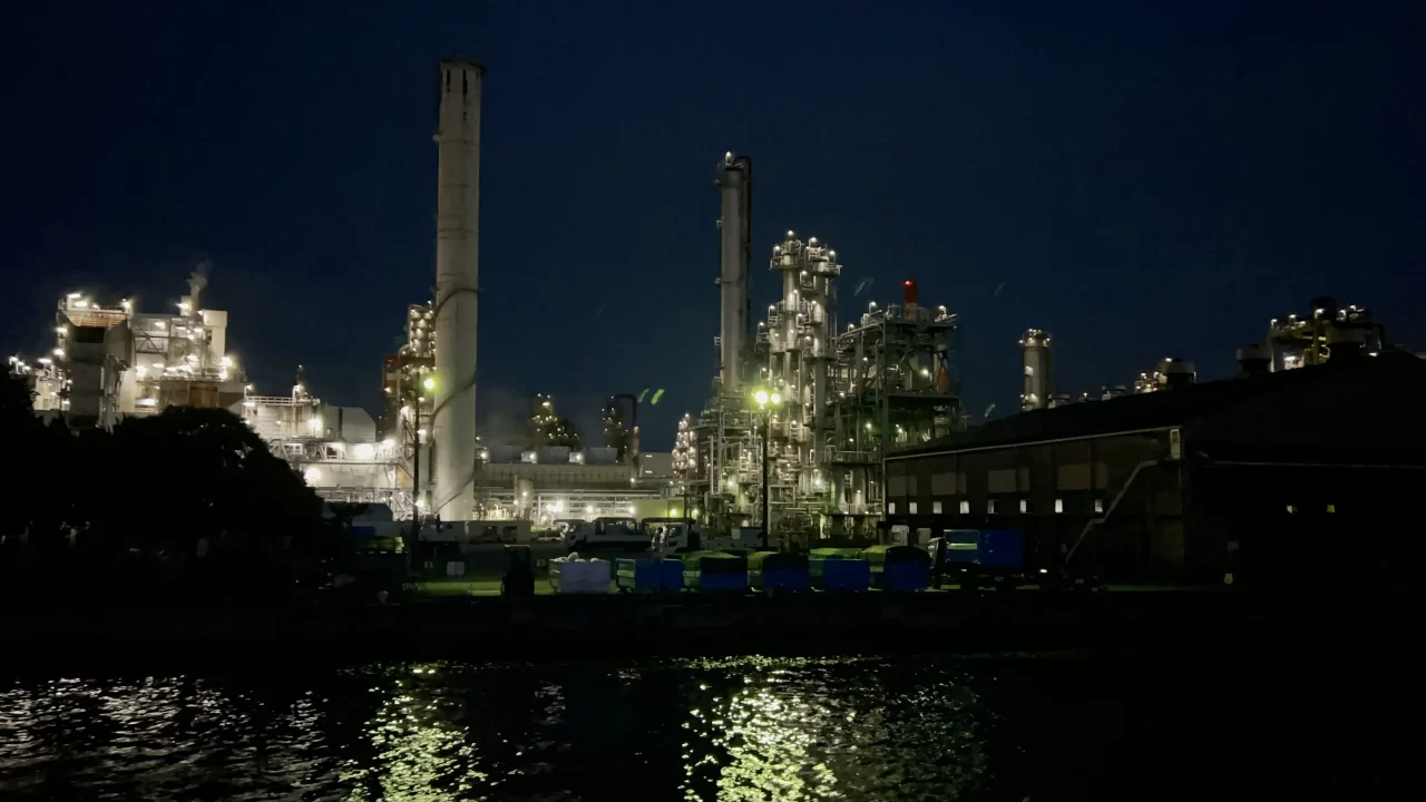 Photo of the Keihin Industrial Zone outside the port of Yokohama. Factories glow with tall, glowing smokestacks. 