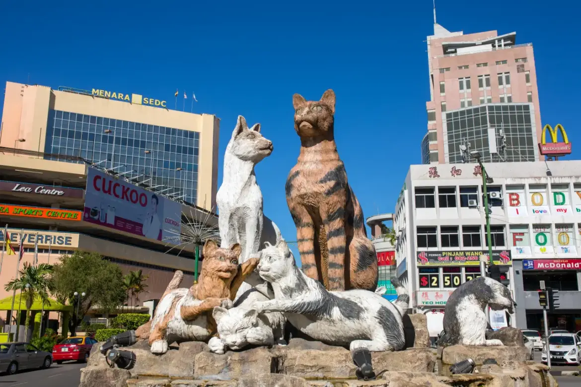 Agoda Lists Asia’s Top Cat-Friendly Travel Destinations Statue of multiple cats in Kuching, Malaysia, known as the “City of Cats,” with commercial buildings and signs in the background.