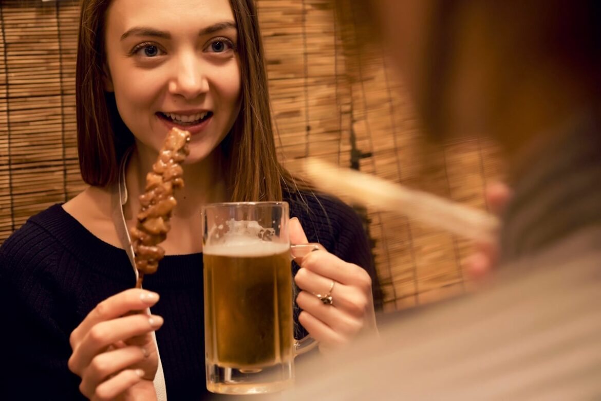 A woman eating kushiyaki and drinking a beer at a restaurant