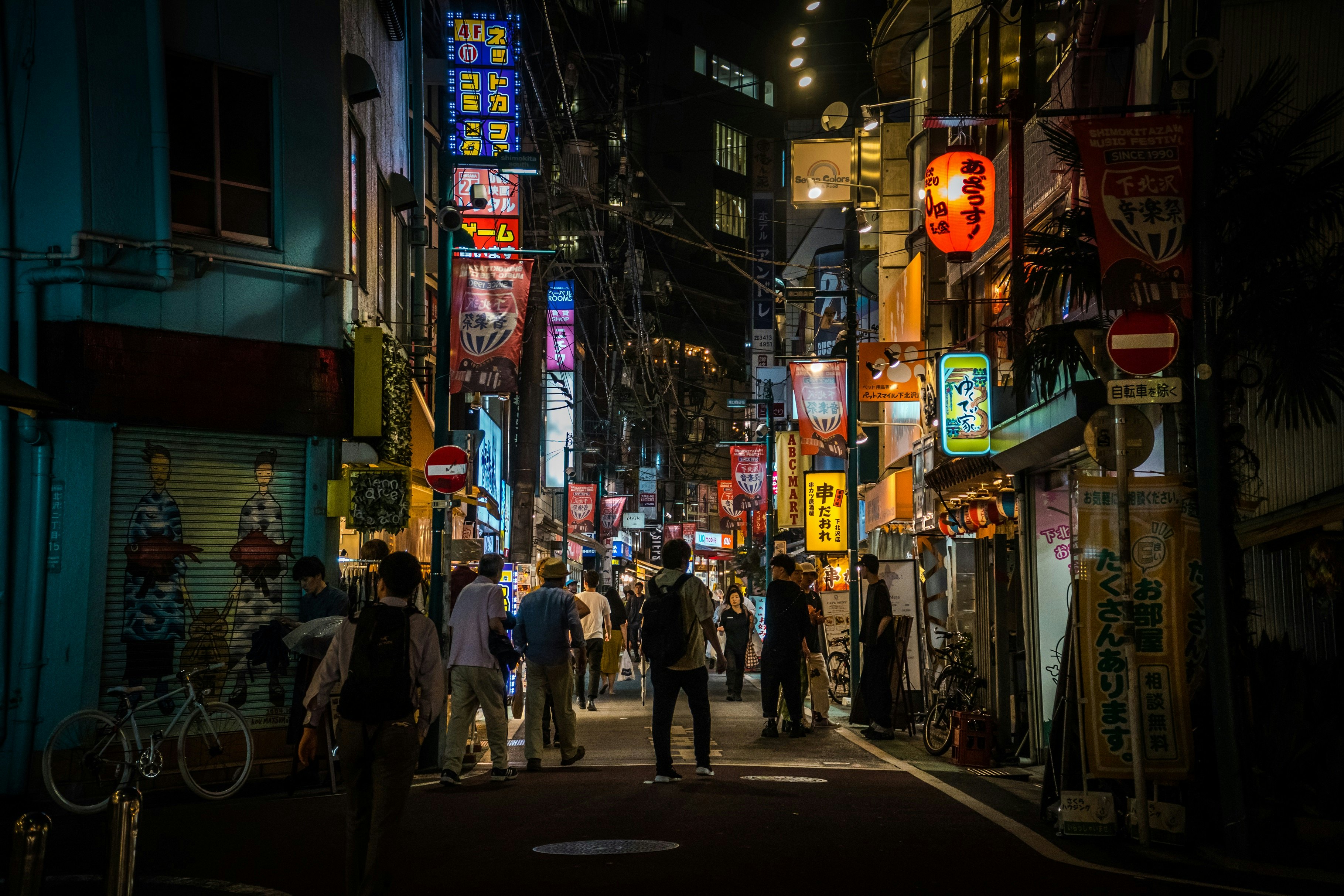 People in a street in the Shimo-kitazawa district of Tokyo at night; neon lights are on the buildings.