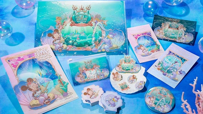 Assorted Disney-themed ocean merchandise, including folders, pouches, plates, and buttons on a blue background.