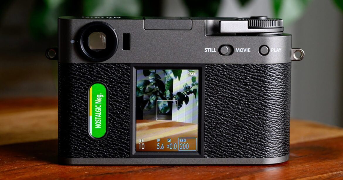 Fujifilm X half Is Yet Again the Best-Selling Camera in Japan (By a Lot) A close-up of the back of a digital camera with a textured black grip, displaying a screen showing a photo of leafy plants and camera settings, and a green button labeled "NOSTALGIC Neg." on the left side.