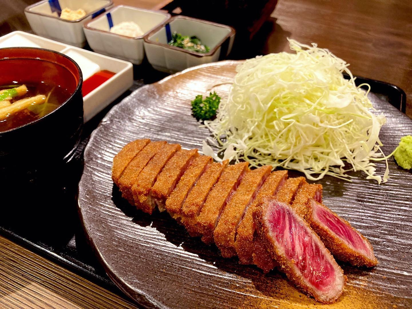 Gyukatsu Motomura's gyukatsu, a Japanese deep-fried beef cutlet, served with shredded cabbage and various side dishes.