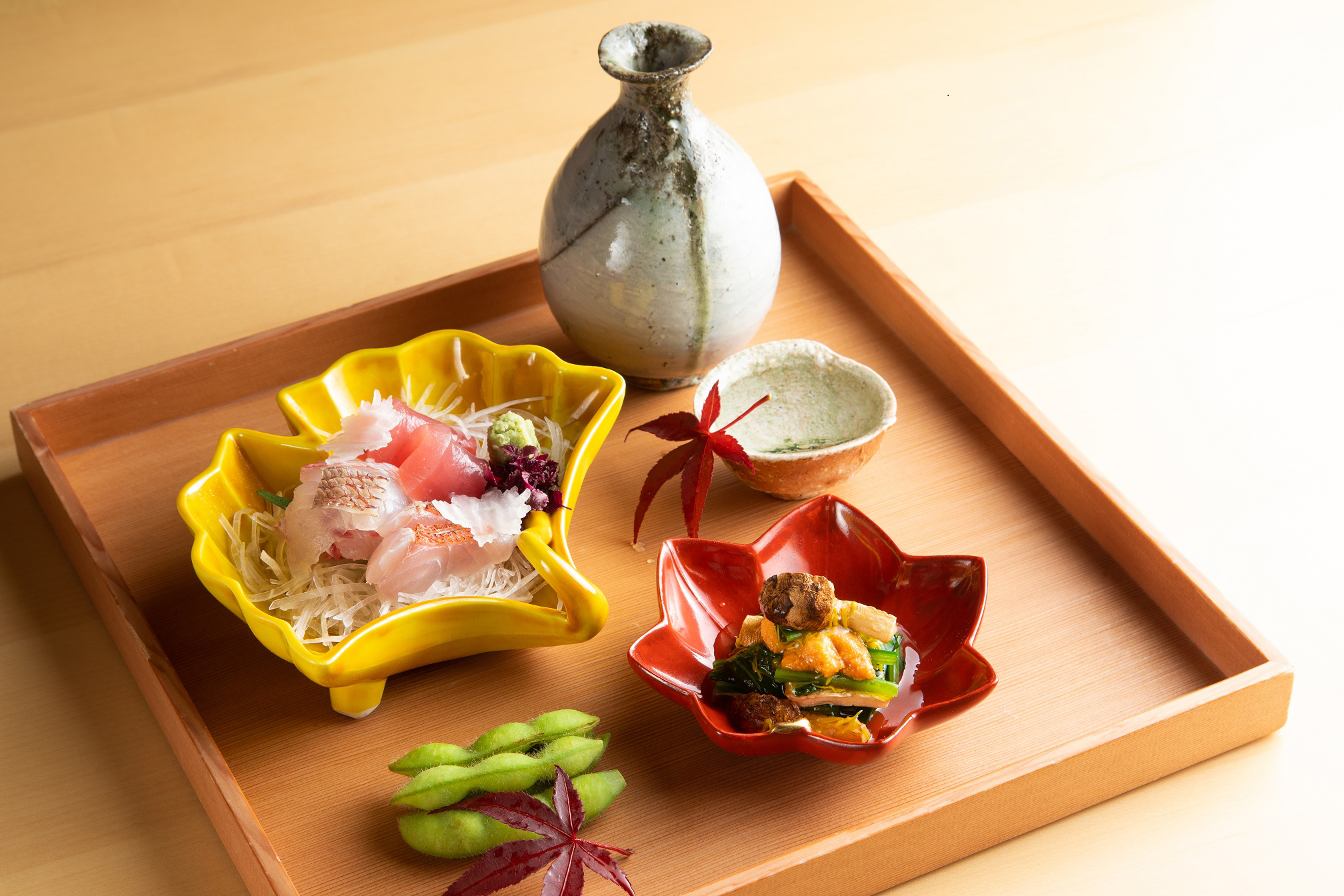 Japanese dinner with sashimi, edamame, and a sake decanter on a wooden tray.