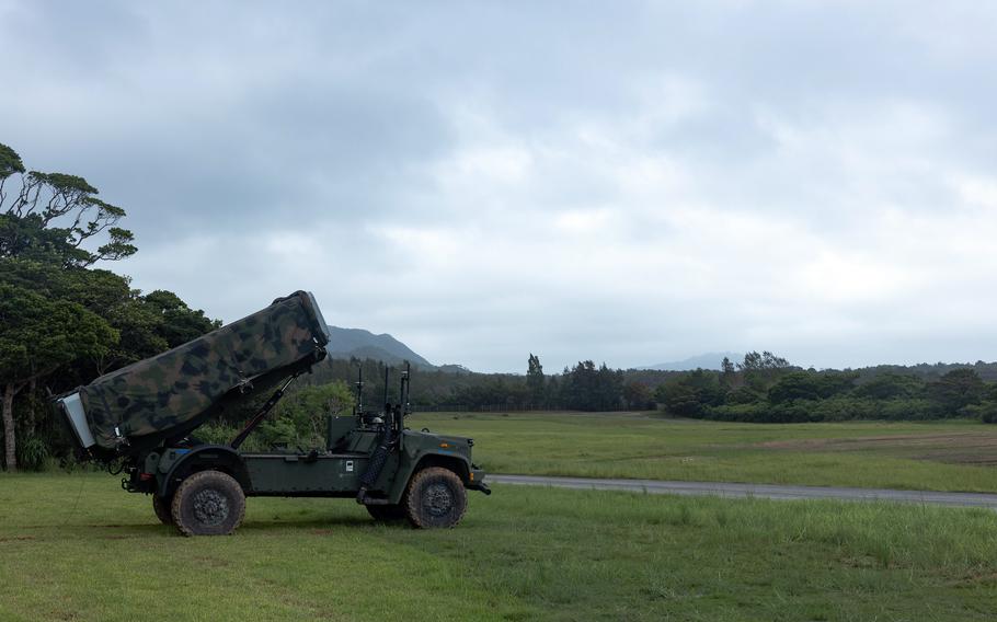 A military missile defense system mounted on a camouflaged truck positioned in a grassy field, with mountains and forest visible in the background under an overcast sky.