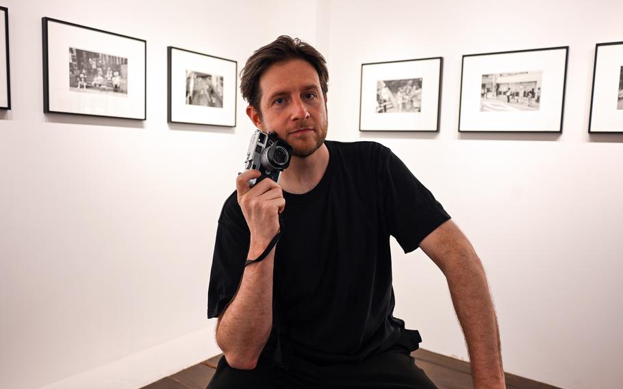 A man sits in a photography museum display room holding a camera.