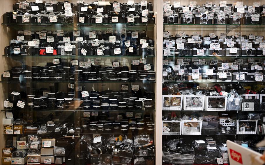 A wall displays a jumble of cameras and camera parts.