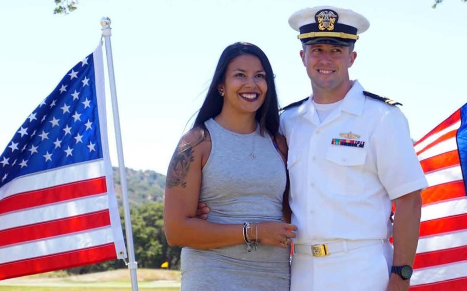 Lt. Cmdr. Christopher Olsen and his wife pose for a photo in front of American flags.