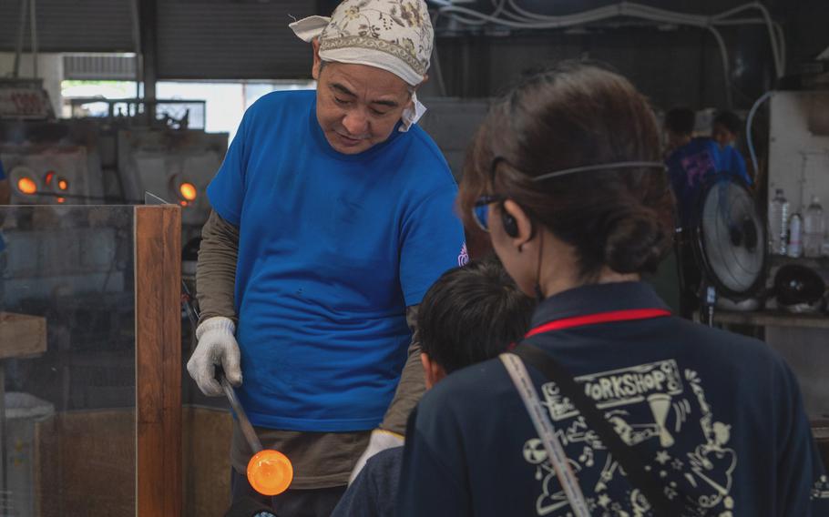 A glass craftsman handles molten glass as spectators watch.
