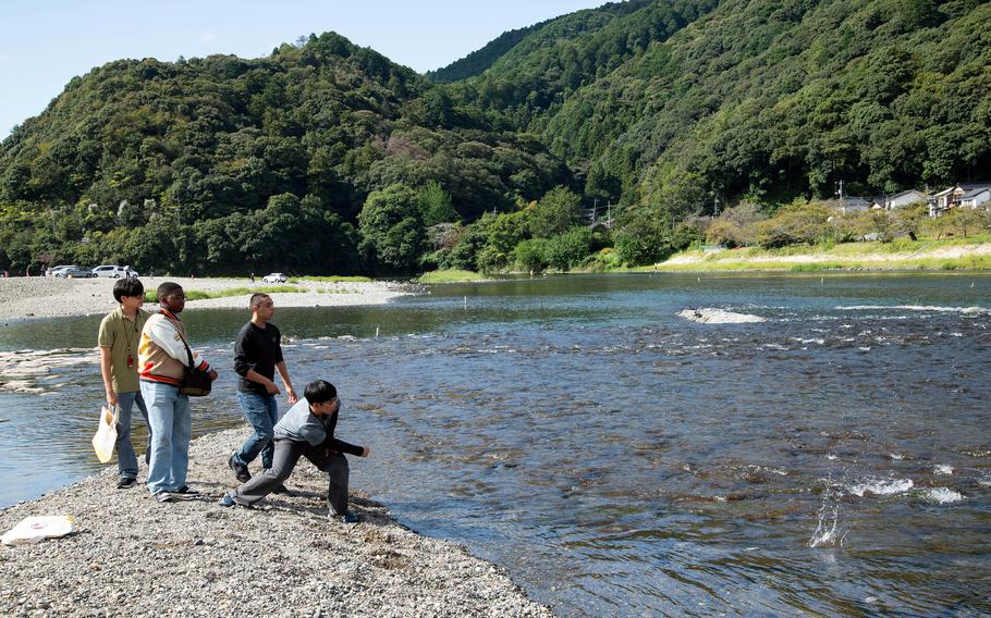 Four boys skip rocks, with one rock making a big splash in the water.