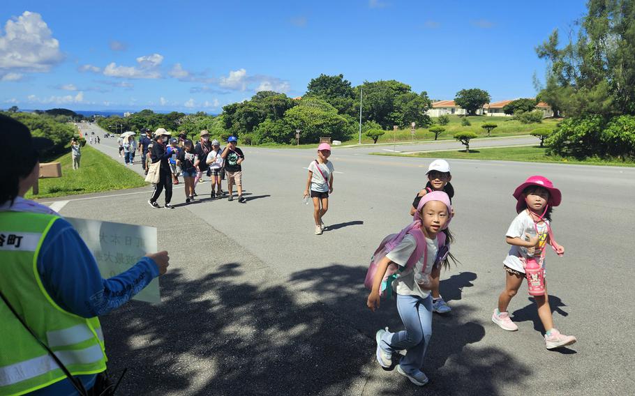 Children wearing hats and water bottles practice walking through a tsunami evacuation drill.