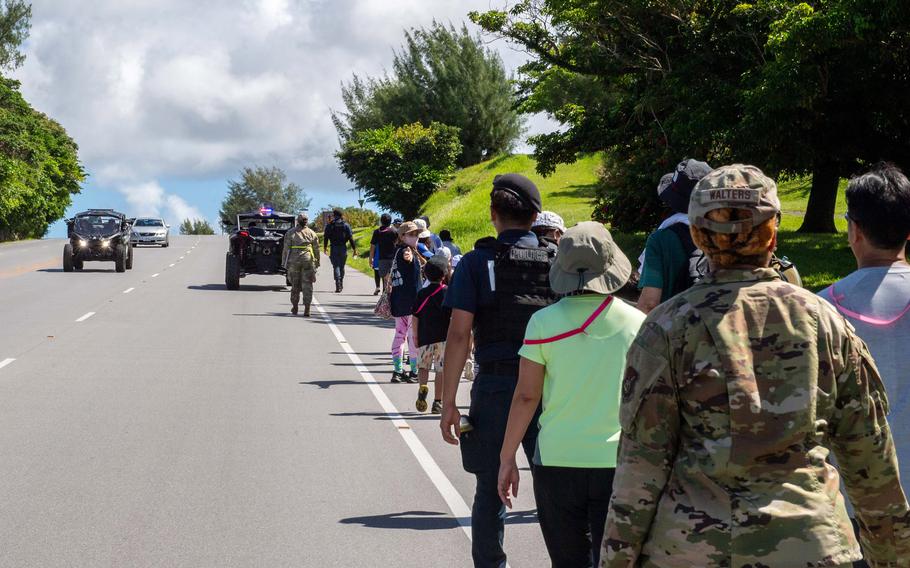 People guided by service members walk down a road.