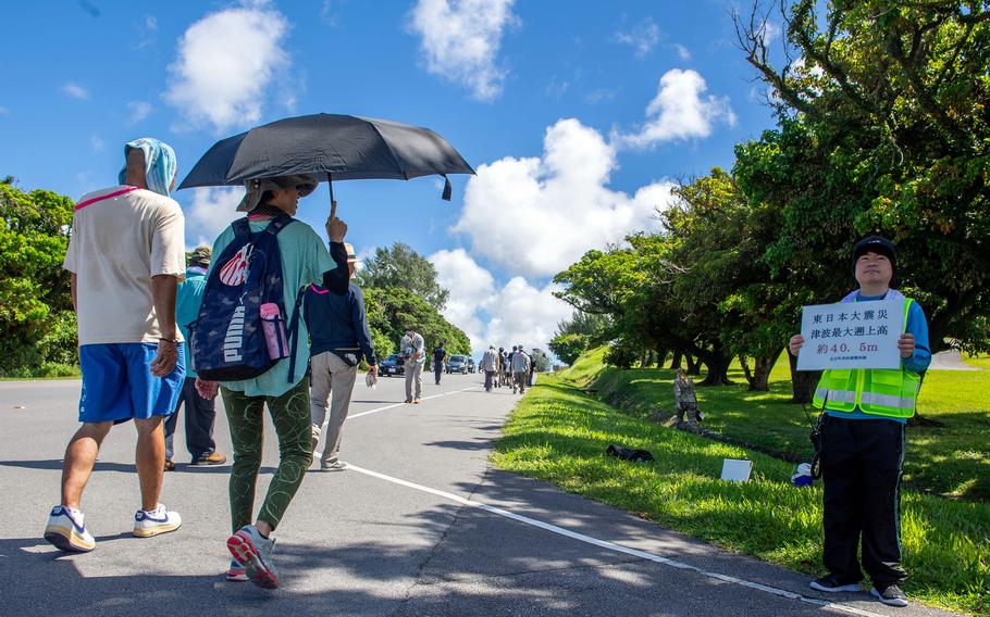 A volunteer wearing a safety jacket and holding a sign directs walkers during a tsunami evacuation exercise.