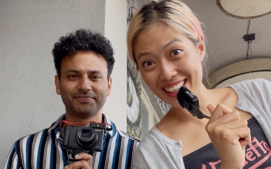 A woman holding a microphone in front of her stands next to a man holding a camera.