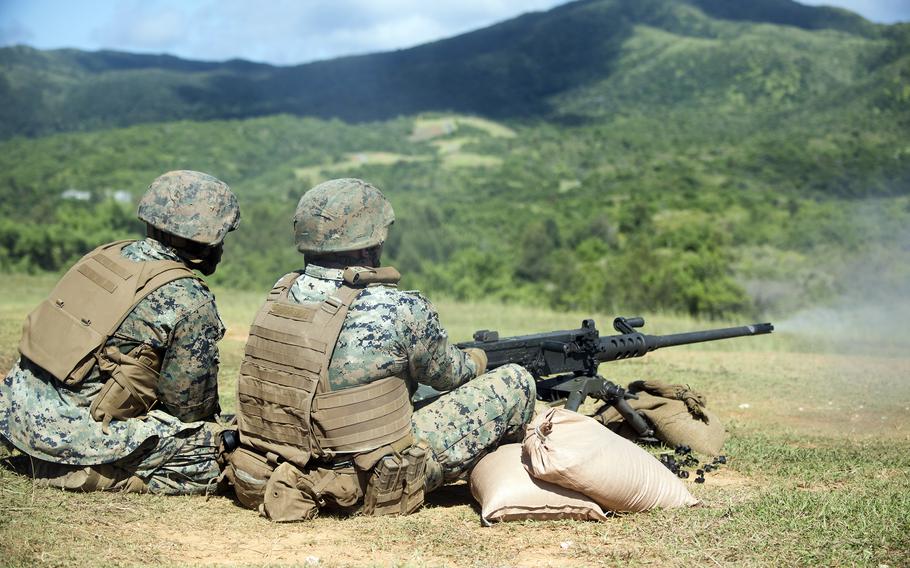 
Two Marines in digital camouflage uniforms and tactical vests while one operates a machine gun during outdoor training. 