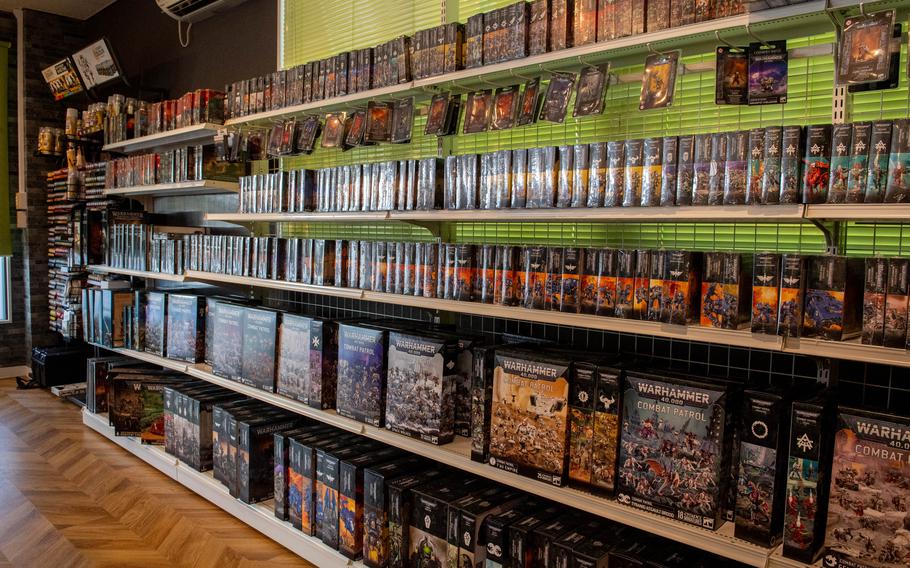 A long row of bookshelves holds items related to the game Warhammer.
