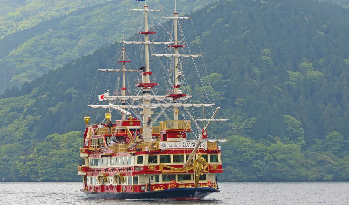 A multi-colored pirate ship cruises on Lake Ashi, with lush forests in the background
