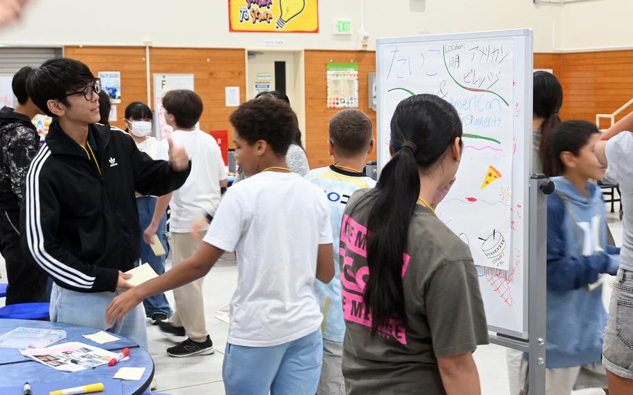 American and Japanese middle school students stand in a school room and work on poster boards.