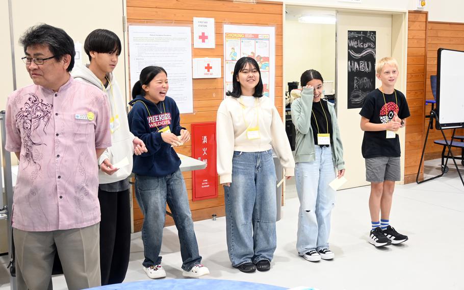 A middle school girl laughs as she stands in a line with other students, rehearsing a presentation.