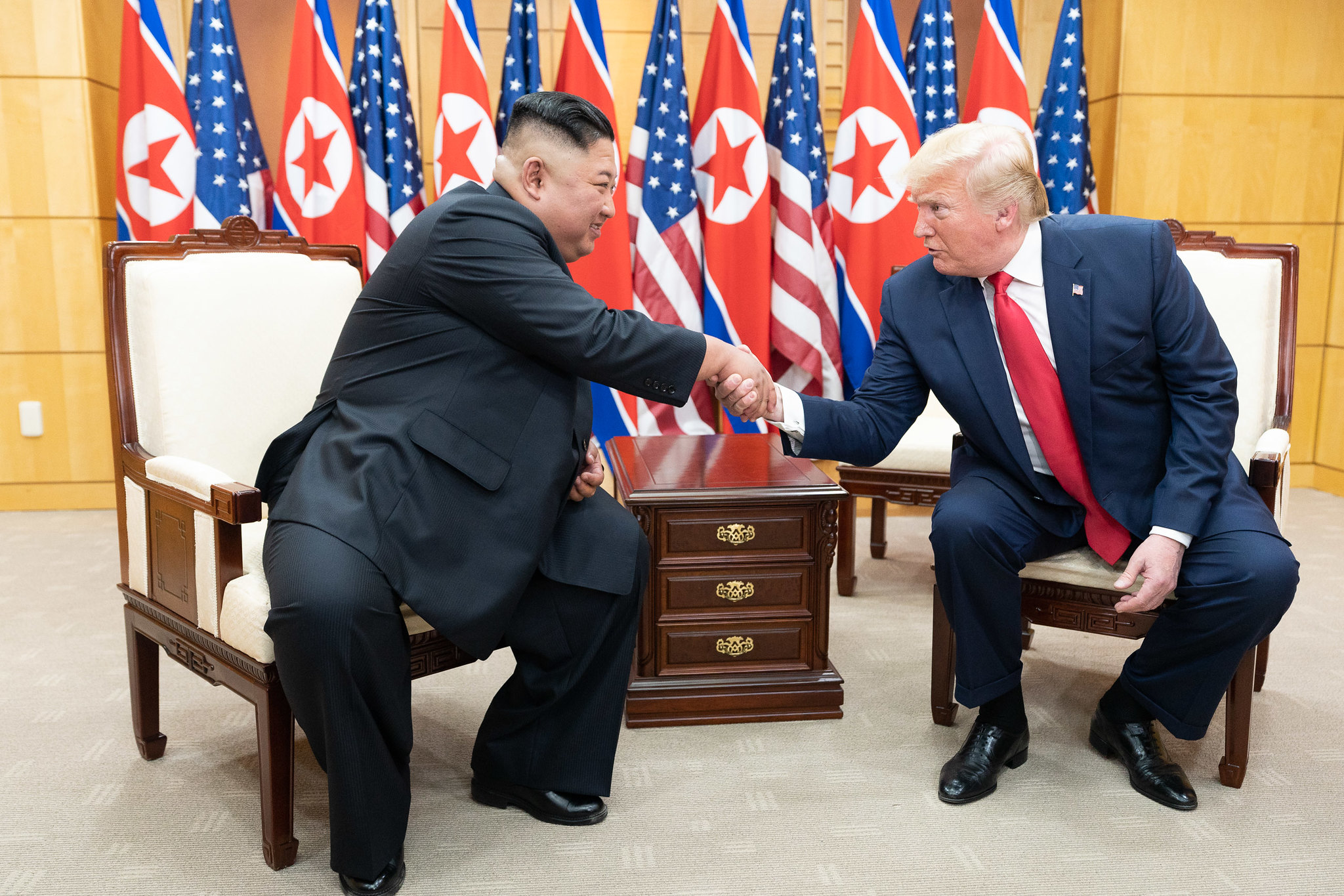 Kim Jong-un shakes hands with Donald Trump in front of US and North Korean flags in a meeting room at the DMZ on the North and South Korean border (Shealah Craighead/White House Photo)