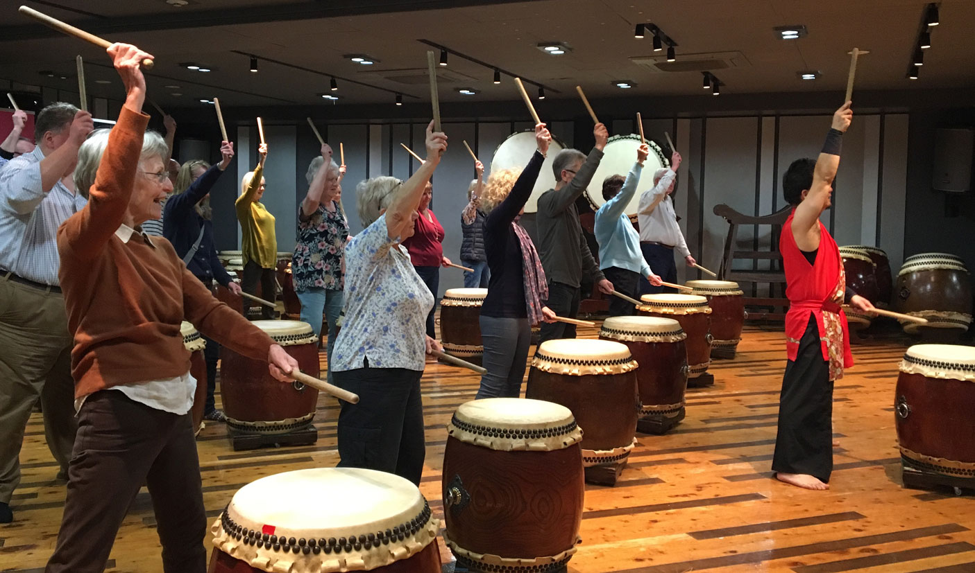 Western tourists copy the moves of a teacher when practicing Taiko drumming