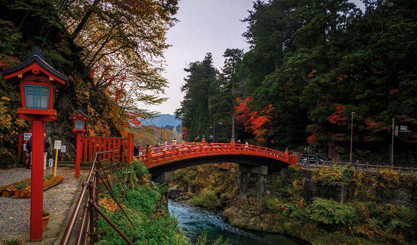 Red bridge over river in Nikko, with red autumn colors in the forest