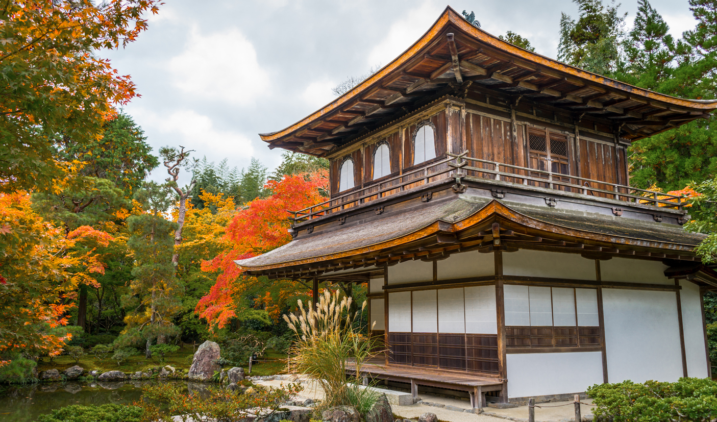 The wooden structure of Ginkaku-ji temple contrasts against a backdrop of red autumn leaves in Kyoto