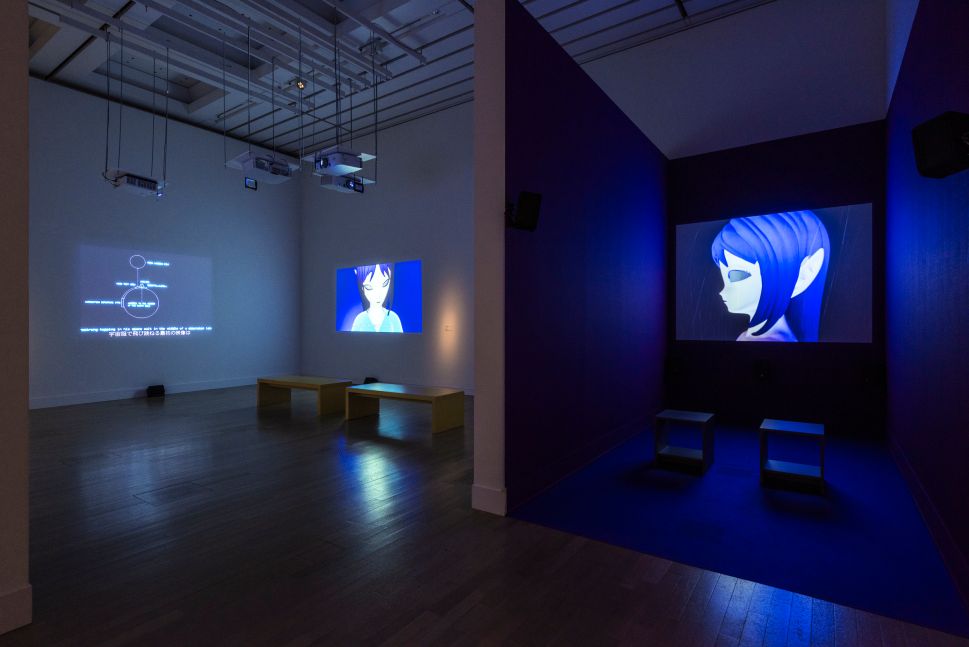 A darkened gallery with multiple video projections of anime-style animated figures, including a large screen showing a blue-haired character’s face.