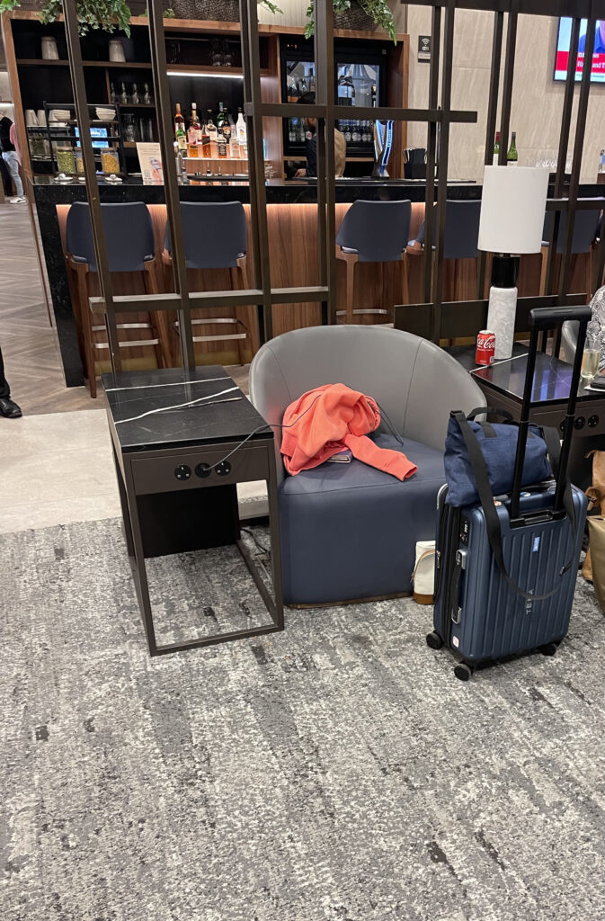The author's luggage is sitting next to a large gray armchair in the Singapore Airlines lounge at Heathrow.