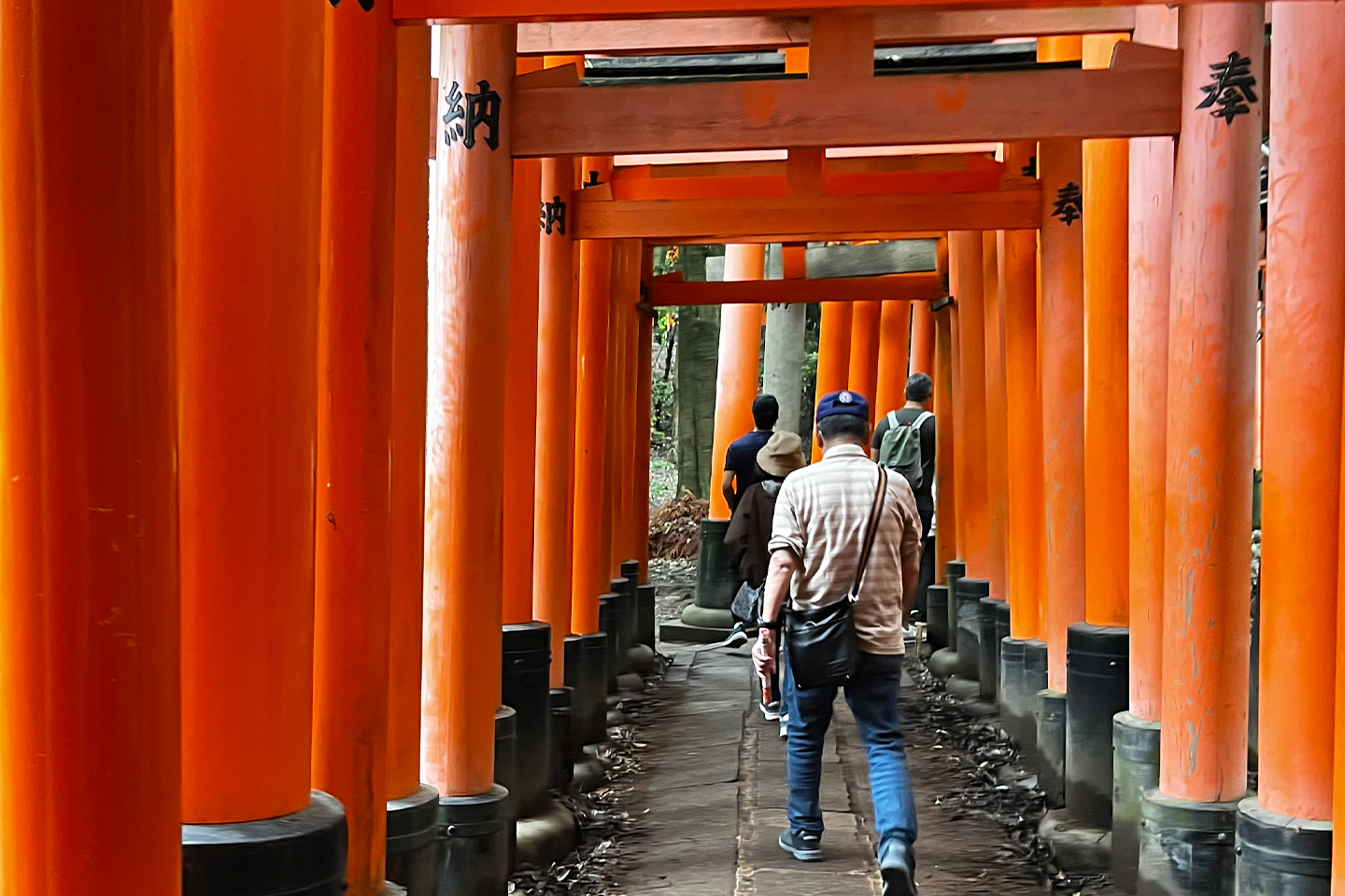Students walking single file through a series of large orange pillars in Japan.