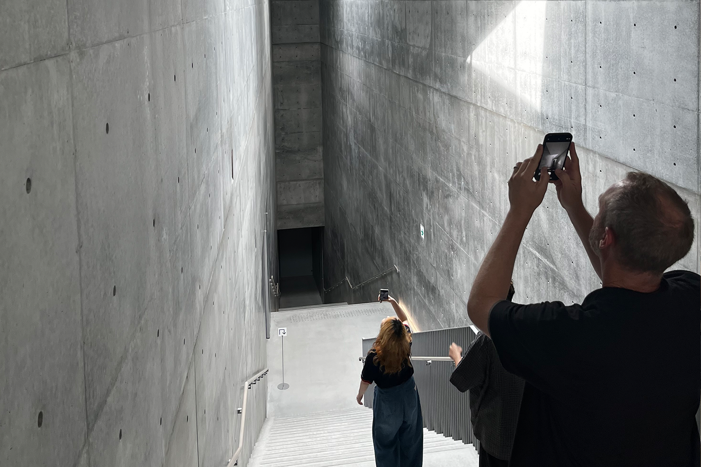 Rick Sommerfeld and a student take photos of the ceiling in a large concrete staircase. 