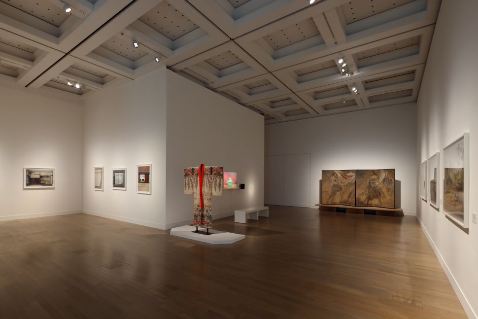 A gallery room with framed photographs of minimalist interiors, a traditional kimono on display, and folding screen paintings against the wall.