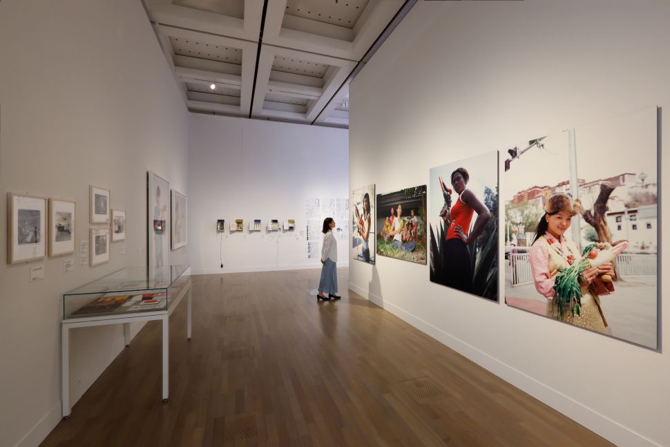 A visitor observing large color photographs of women in everyday and performative settings, surrounded by documentary images and display cases.
