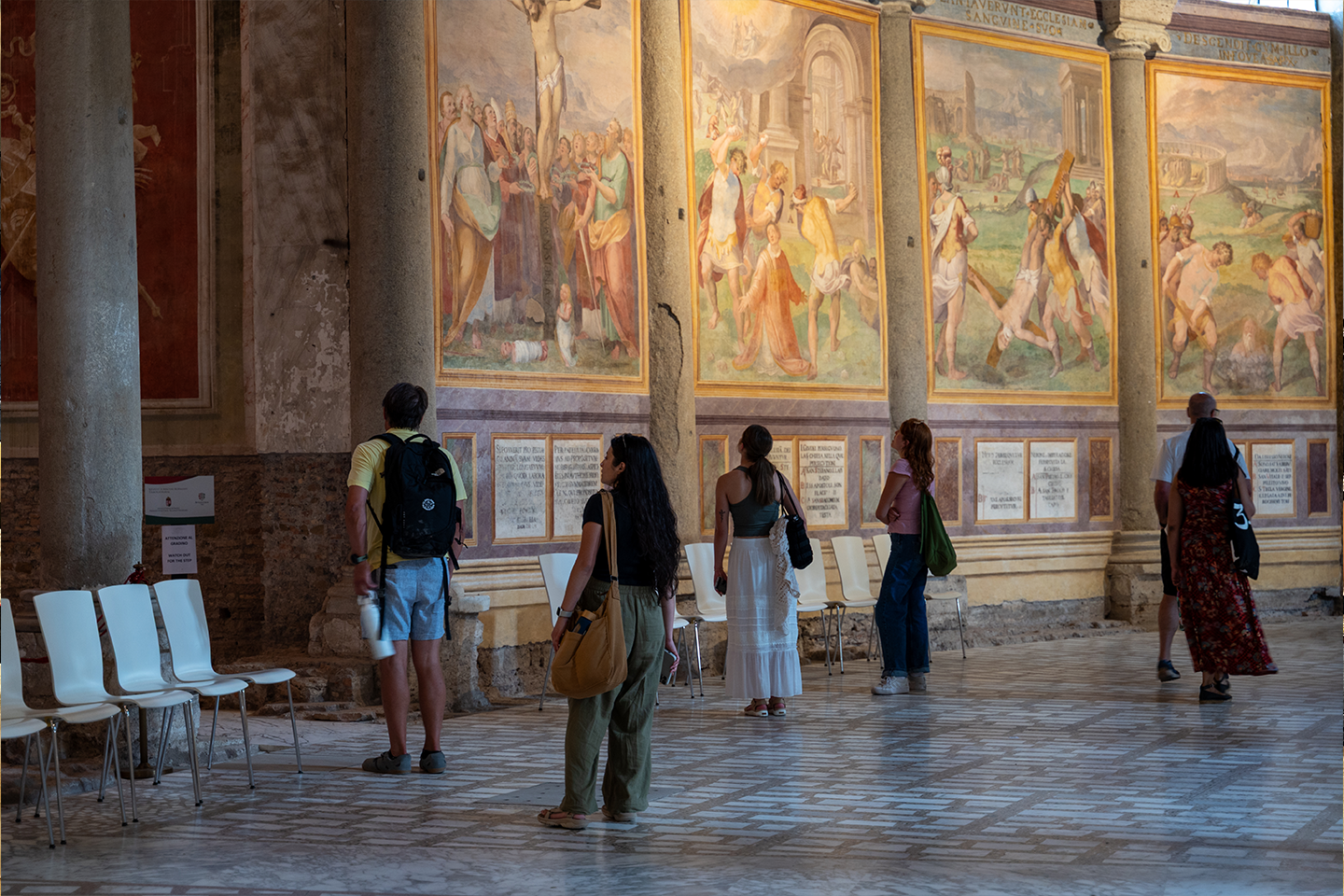 Six people walking through a Roman cathedral and looking at the artwork on the walls. 