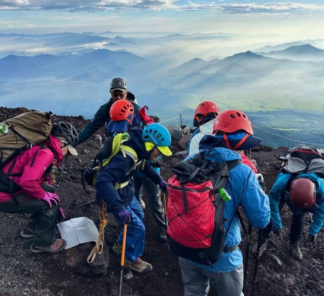 This photo provided by Motoe Hoshino shows her father Kokichi Akuzawa, center in a blue helmet, as they and their climbing friends and other family members were climbing Mount Fuji, west of Tokyo, Aug. 5, 2025. (Family courtesy photo via AP)