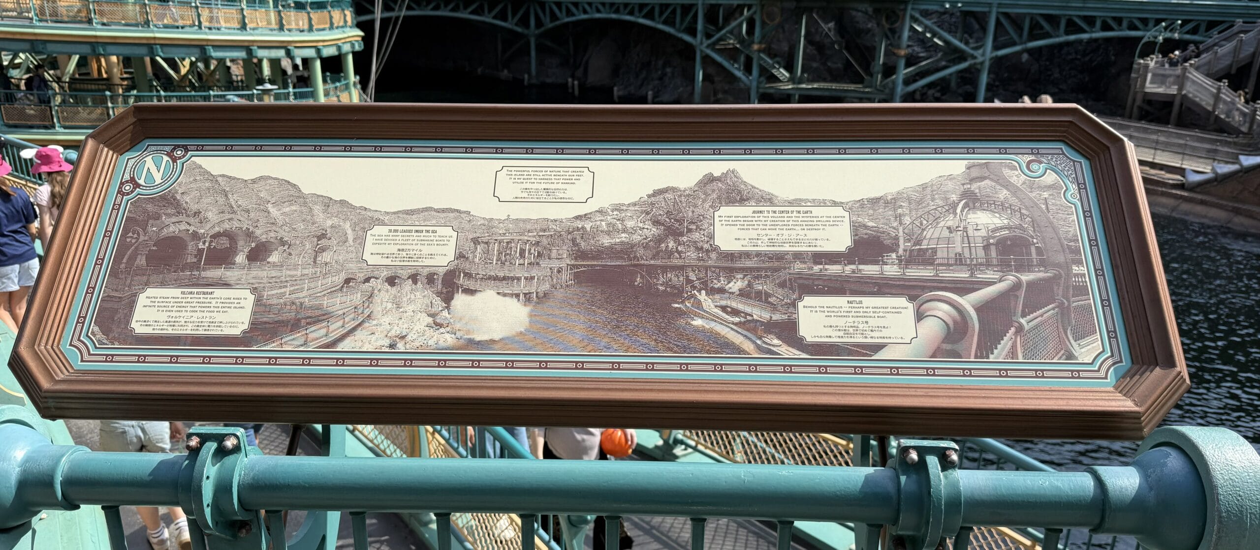 A panoramic information sign describes points of interest in a themed waterfront area with rocky and architectural features.