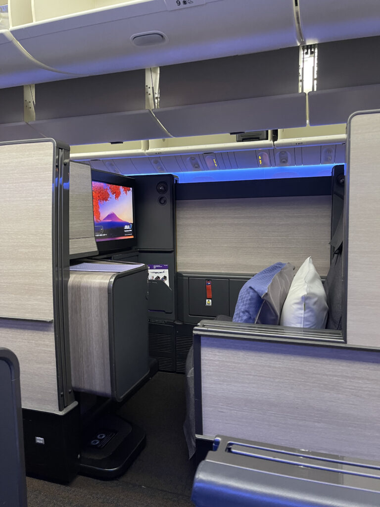 From the outside of the ANA business class seat, looking in at an all grey seat in a suite with black trim and finishings.