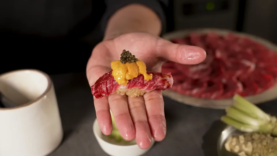 A hand holding nigiri made with wagyu beef.