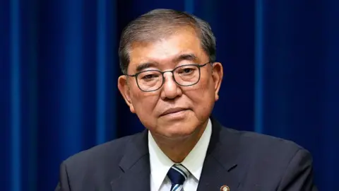 Getty Images Japan's Prime Minister Shigeru Ishiba wearing a dark suit stands in front of blue curtains