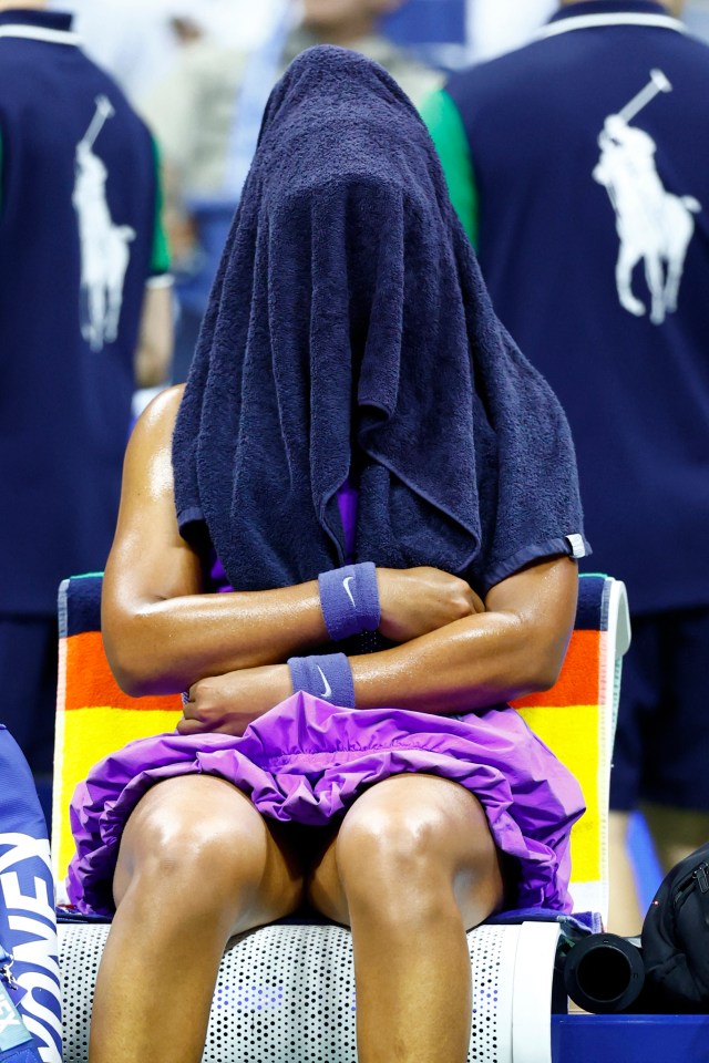 Naomi Osaka sits with a towel over her head during a break in a tennis match.