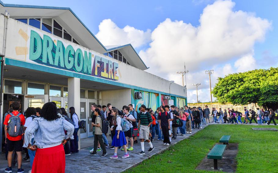 A large group of students with backpacks gather outside a two-story school building with “DRAGONFIRE” signage in teal and purple letters above the entrance.