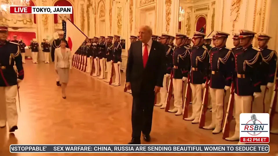 A formal ceremony in a grand hall with uniformed guards and a man in a suit with a bright tie, featured on a TV broadcast labeled "Tokyo, Japan."