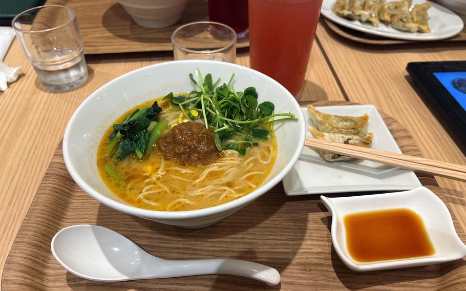 A bowl of ramen includes a vegan meatball and greens.