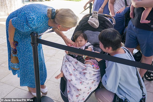 The Duchess of Edinburgh is pictured stroking a baby's cheek as she meets with members of the public